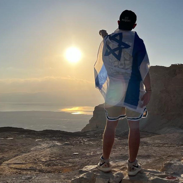 Jewish boy looking out at the sunset on top of Masada wearing the Israeli flag. 